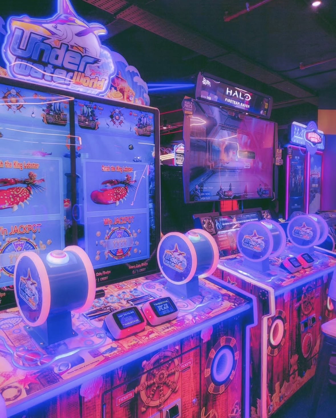 A neon-lit arcade with an Underwater World ticket machine and a Halo cabinet glowing pink and blue
