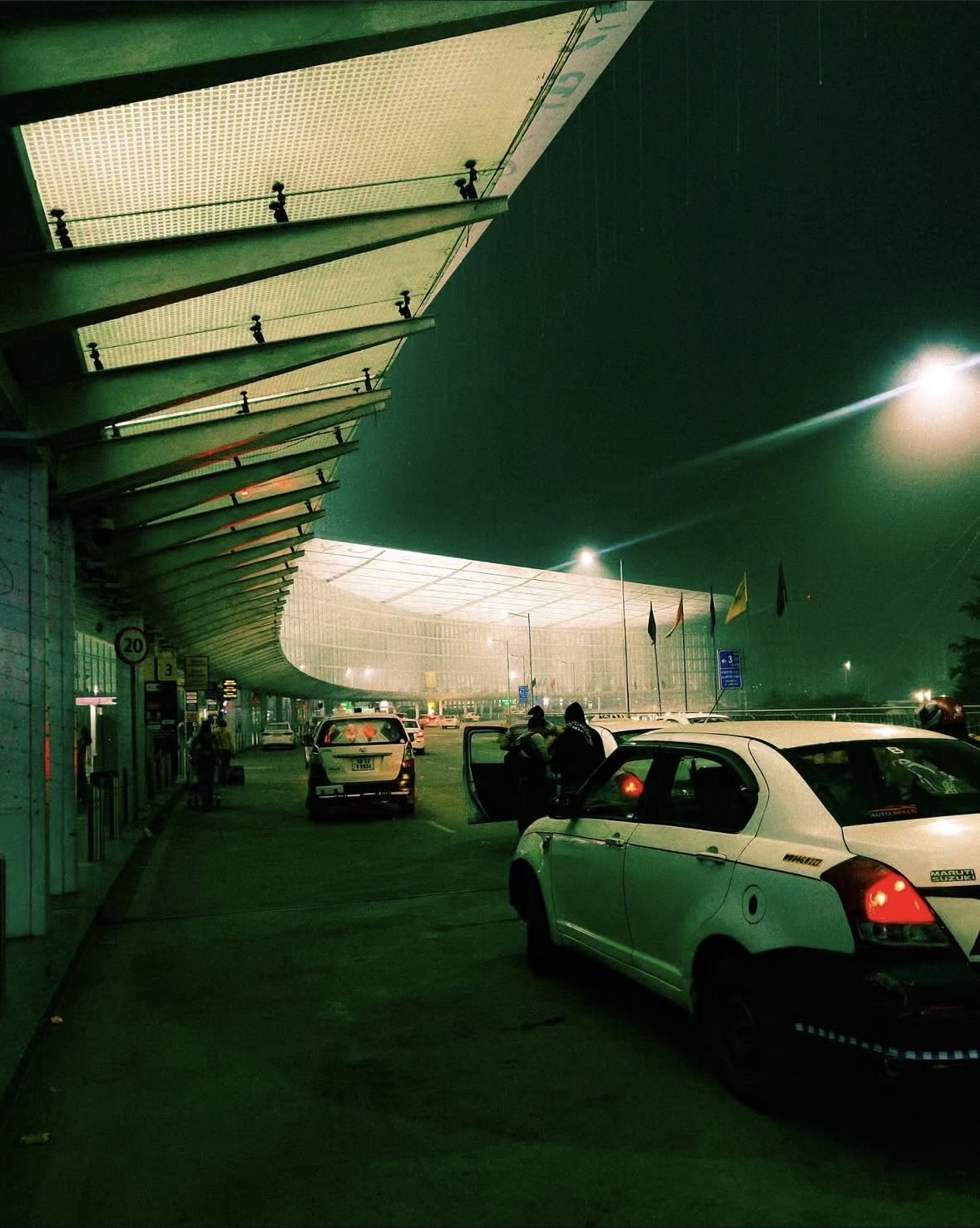 Taxis waiting under the curved canopy of an airport terminal on a wet night
